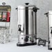 A Town 10 liter water boiler on a table with a group of glass cups and silver containers.