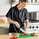 A woman in a black Uncommon Chef cook shirt cutting peppers.