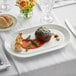 An Acopa Liana bright white porcelain platter with a piece of meat and vegetables on it with a knife.