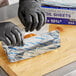 A person wearing black gloves using Choice Blue Striped Interfolded Foil to pack food.