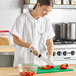A woman in a white Uncommon Chef cook shirt cutting peppers.