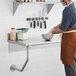 A man in a brown apron mixing food on a Regency stainless steel wall mounted table.