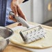 A person using an American Metalcraft dough docker with a cast aluminum handle to make pizza dough.