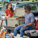 A man and woman sitting on the back of a truck with a CaterGator outdoor cooler.