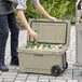 A man in black pants puts beer bottles and cans in a tan CaterGator outdoor cooler.