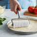 A hand using an American Metalcraft pizza dough docker with a cast aluminum handle to roll out pizza dough.