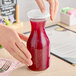 A hand holding a Choice polycarbonate carafe filled with red liquid.