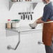 A man in a brown apron mixing food on a Regency stainless steel wall mounted table.