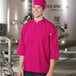 A man wearing a pink Uncommon Chef 3/4 length sleeve chef coat with side vents.