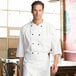 A man in a Uncommon Chef white 3/4 sleeve chef coat standing in a professional kitchen.