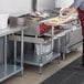 A woman in a red apron using a Regency stainless steel equipment stand with wooden cutting board to prepare food.