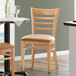 A Lancaster Table & Seating wooden ladder back chair with a light brown vinyl seat at a table in a restaurant.