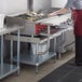 A woman in a red apron using a Regency stainless steel equipment stand in a commercial kitchen.