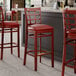 A group of Lancaster Table & Seating mahogany wood bar stools with burgundy vinyl seats next to a bar counter.