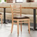 A Lancaster Table & Seating wooden chair with dark brown vinyl seat next to a table.