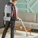 A person with a ProTeam cordless backpack vacuum cleaning a carpet.