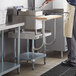 A man in a commercial kitchen using a Regency stainless steel equipment stand with a wooden cutting board.