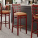 A group of Lancaster Table & Seating mahogany wood window back bar stools with light brown vinyl seats next to a counter.