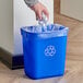 A person putting a plastic bag into a blue Continental Recycling Wastebasket with a recycle symbol on it.