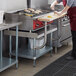 A woman in a kitchen uses a Regency stainless steel equipment stand with a wooden cutting board.