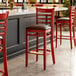 A row of Lancaster Table & Seating mahogany wood bar stools with dark brown vinyl seats in a restaurant.