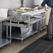 A man in a commercial kitchen using a Regency stainless steel equipment stand with a grill on the counter.