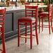 A Lancaster Table & Seating mahogany wood ladder back bar stool with a burgundy vinyl seat.