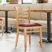A row of Lancaster Table & Seating wooden restaurant chairs with burgundy vinyl seats.