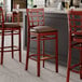 Three Lancaster Table & Seating mahogany wood bar stools with dark brown vinyl seats next to a counter.