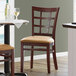 A Lancaster Table & Seating wood window back chair with a light brown vinyl seat at a table in a restaurant.