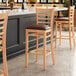 A Lancaster Table & Seating wood bar stool with a dark brown vinyl seat.