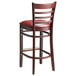 A Lancaster Table & Seating mahogany wood bar stool with burgundy vinyl seat and ladder back.