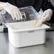 A person in gloves and a white apron putting a Carlisle plastic lid on a food container.