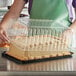 A woman using a Choice 1/4 Size High Dome Sheet Cake Display Container with clear lid to hold a frosted cake.