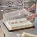 A person in a white apron holding a Choice plastic container with a cake inside.