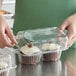 A person holding a Choice plastic container with a jumbo cupcake inside.