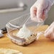 A person in gloves cutting a cake in a Choice clear plastic container with a medium dome lid.