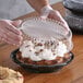 A person in gloves putting a clear plastic lid on a cake in a black plastic container.