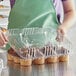 A woman in an apron putting plastic container of cupcakes on a bakery display counter.