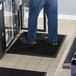 A person standing on a black rubber anti-fatigue mat in front of a refrigerator.