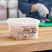 A woman in blue gloves using a Araven translucent plastic food pan to cut potatoes on a counter.