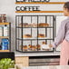 A three-tier bakery display case with a black frame and glass panels, containing assorted pastries.