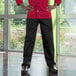 A man in a black classic chef pants and red shirt standing in a professional kitchen.