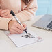 A person using a Quartet white glass dry erase notepad to write on a piece of paper on a table.