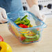 A person in gloves using an Araven blue plastic food pan to store yellow and green peppers.