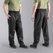 The legs and torso of a man wearing Uncommon Chef Black Classic Chef Pants with a green shirt.