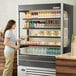 A woman standing in front of a Beverage-Air VueMax air curtain merchandiser filled with juice.