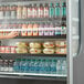 A woman reaching for a Beverage-Air VueMax air curtain merchandiser filled with food.