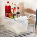 A woman using a red and black Araven shelf ingredient bin to store food in a professional kitchen.