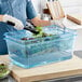 A person in gloves using a blue Araven colander pan to serve lettuce in a container.